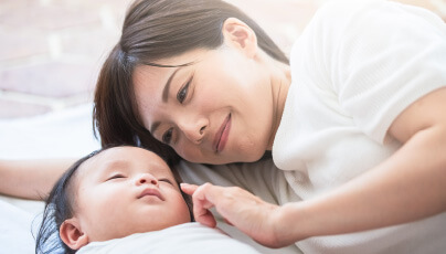 眠っている赤ちゃんを見つめる女性の写真